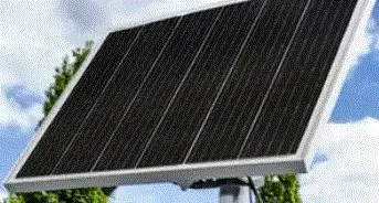 Schwarzes Solarpanel mit Aluminiumrahmen auf einem Mast montiert, vor einem bewölkten Himmel und Bäumen im Hintergrund.