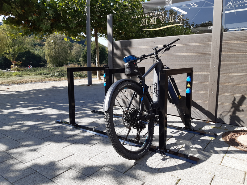Schwarzer E-Bike Anlehnbügel im Außenbereich auf Pflasterfläche montiert, Fahrrad sicher abgestellt, ohne Ladeeinheit