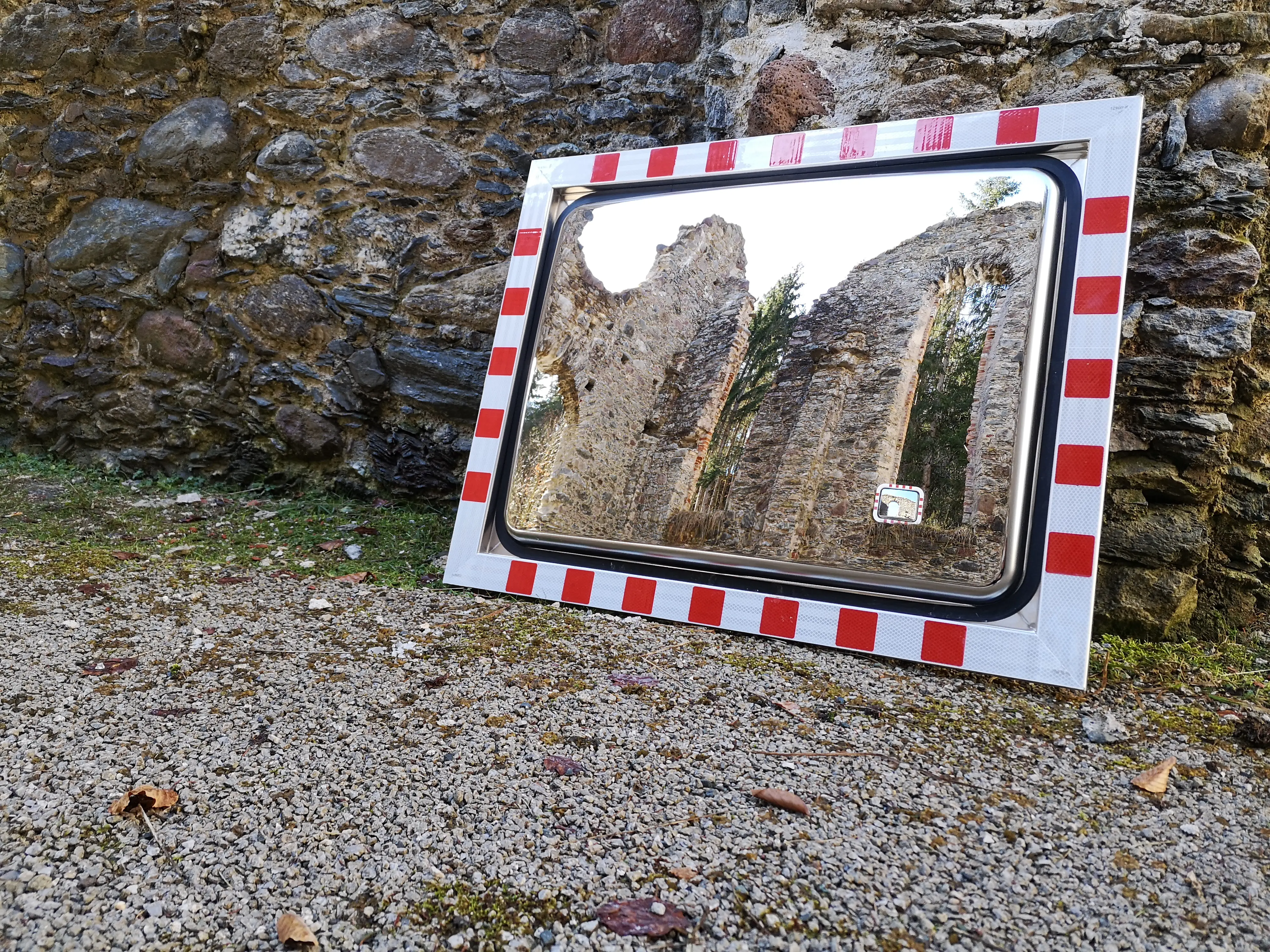 Verkehrsspiegel 600x800 mm mit rot-weißem Rand, gespiegelt ist eine alte Ruine mit Bäumen im Hintergrund
