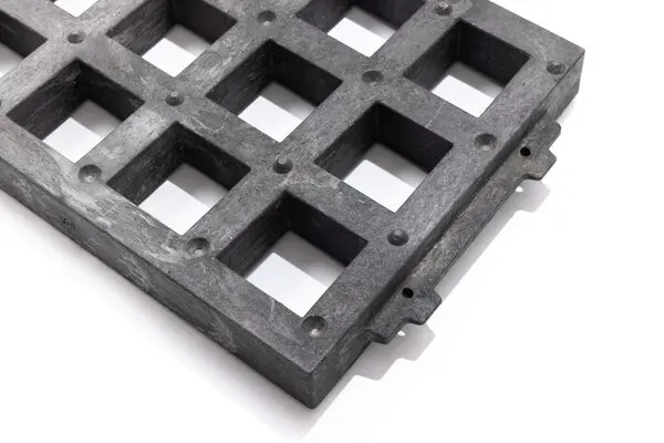 Nahaufnahme eines Rasengittersteins aus schwarzem Kunststoff mit quadratischen Öffnungen und seitlichen Verbindungselementen