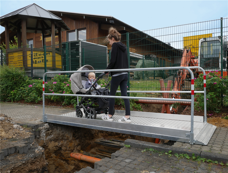 Seitliche Ansicht einer Grabenbrücke mit Geländer und rutschhemmender Oberfläche zur Baustellenüberquerung