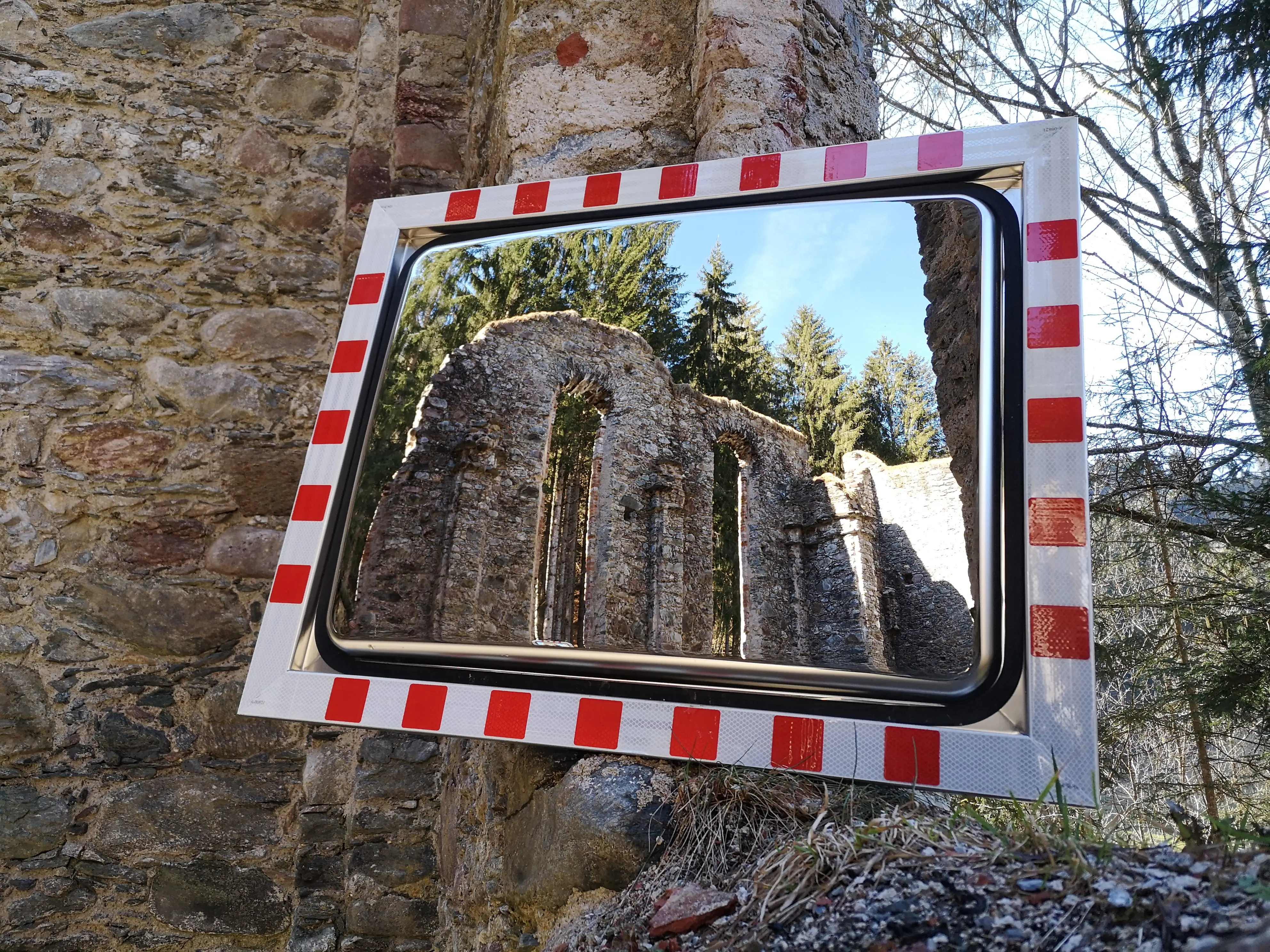 Verkehrsspiegel 600x800 mm mit rot-weiß reflektierendem Rahmen, angelehnt an einer Ruinenmauer