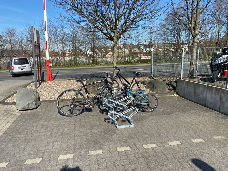 Doppelseitiger Fahrradständer im Außeneinsatz mit mehreren abgestellten Fahrrädern, auf befestigtem Boden vor einem Parkplatzbereich montiert